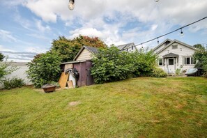 Un jardin à l’arrière d’une maison, avec un abri de jardin, une pelouse et la maison elle-même.