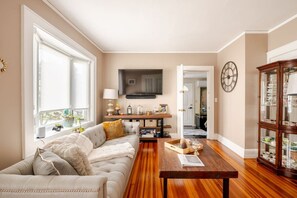 Un salon comprenant un canapé, une table basse, un téléviseur à écran plat, un meuble en bois et une horloge murale.