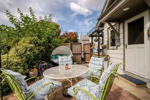 Eine Terrasse mit einem runden Tisch und Stühlen, umgeben von Pflanzen und einem Holzzaun.