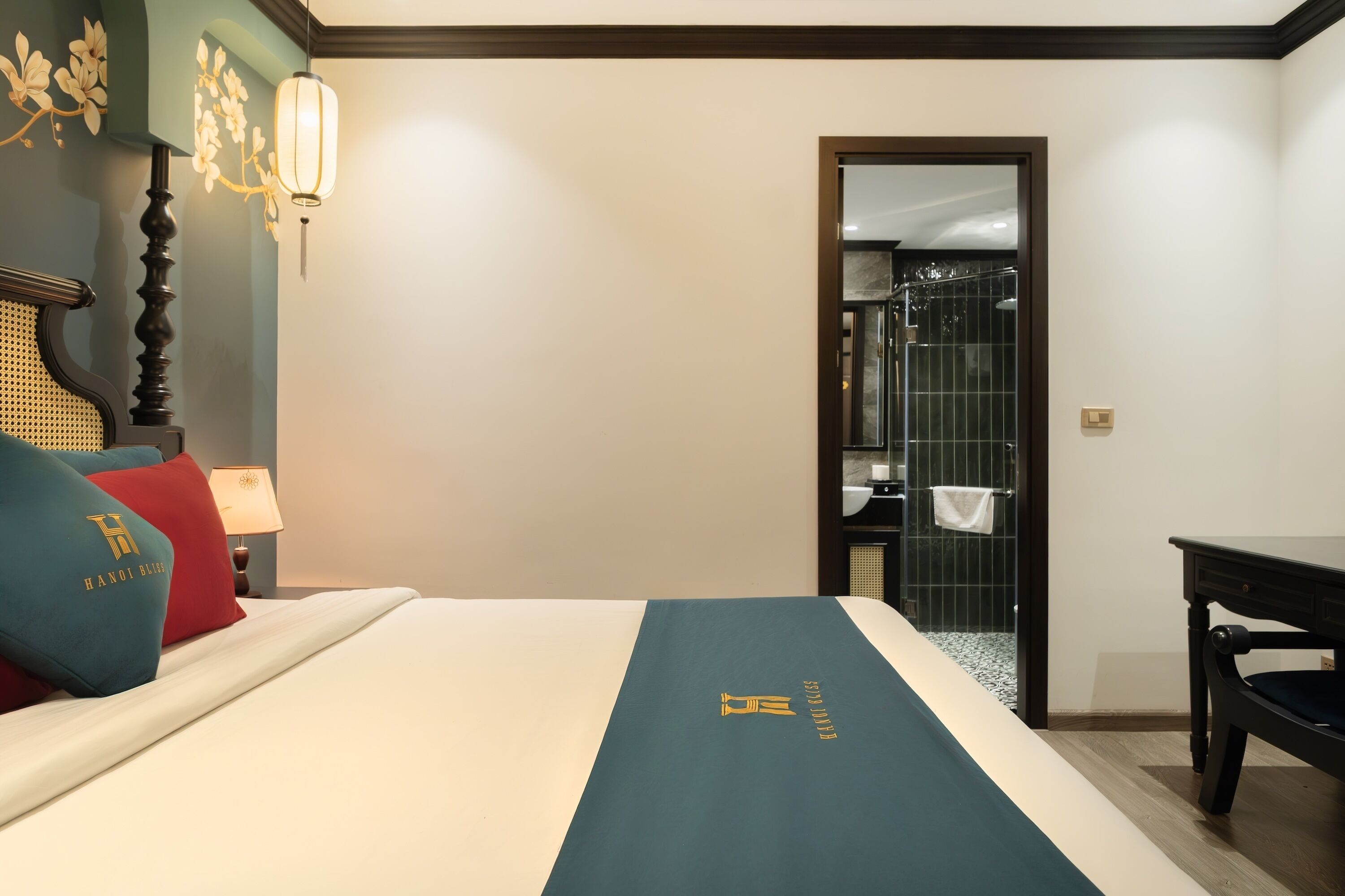 A hotel room with a neatly made bed, a desk, and a bathroom visible through an open door.