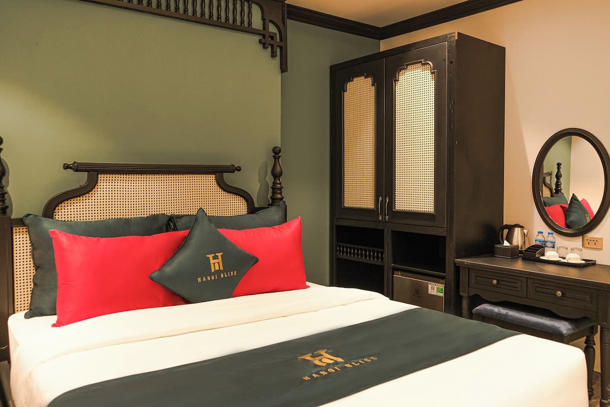 A hotel room with a bed, a wardrobe, a mirror, and a desk with a coffee maker.