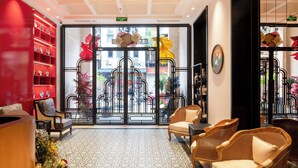 A hotel lobby with a patterned floor, wicker furniture, and a red wall with shelves. - Bliss Signature Hotel (Hanoi)