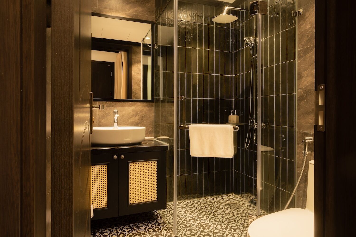 A modern bathroom with a glass-enclosed shower, a sink with a mirror above, and a patterned floor.