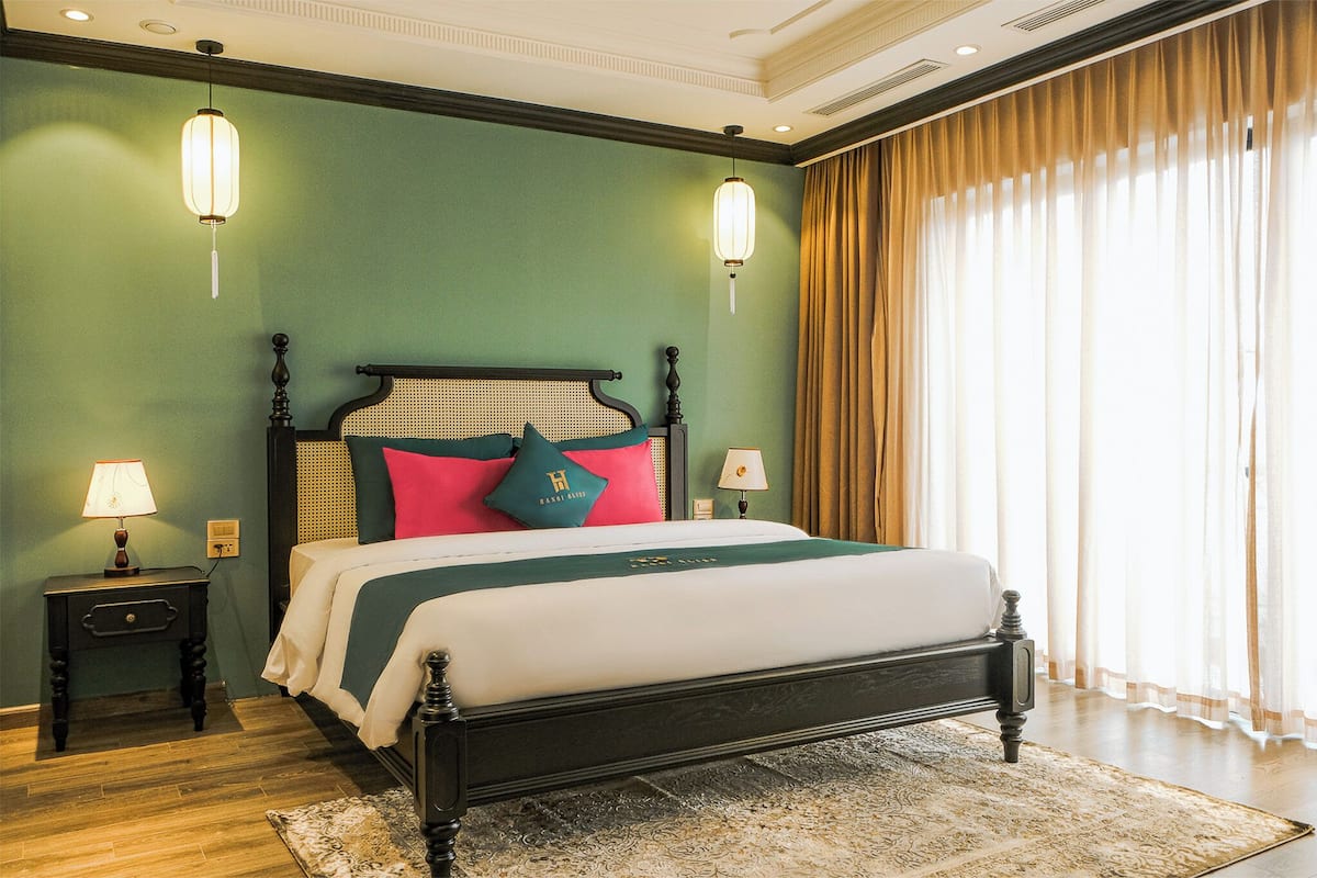 A neatly made bed with a headboard, two bedside tables with lamps, and a large window with sheer curtains.