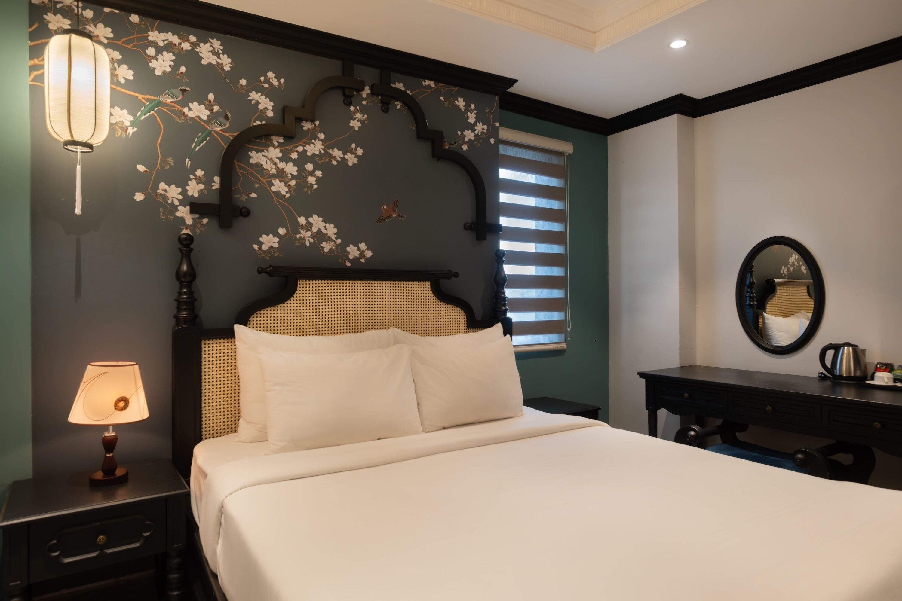 A hotel room with a bed, a nightstand with a lamp, a dresser, and a wall with a floral design.