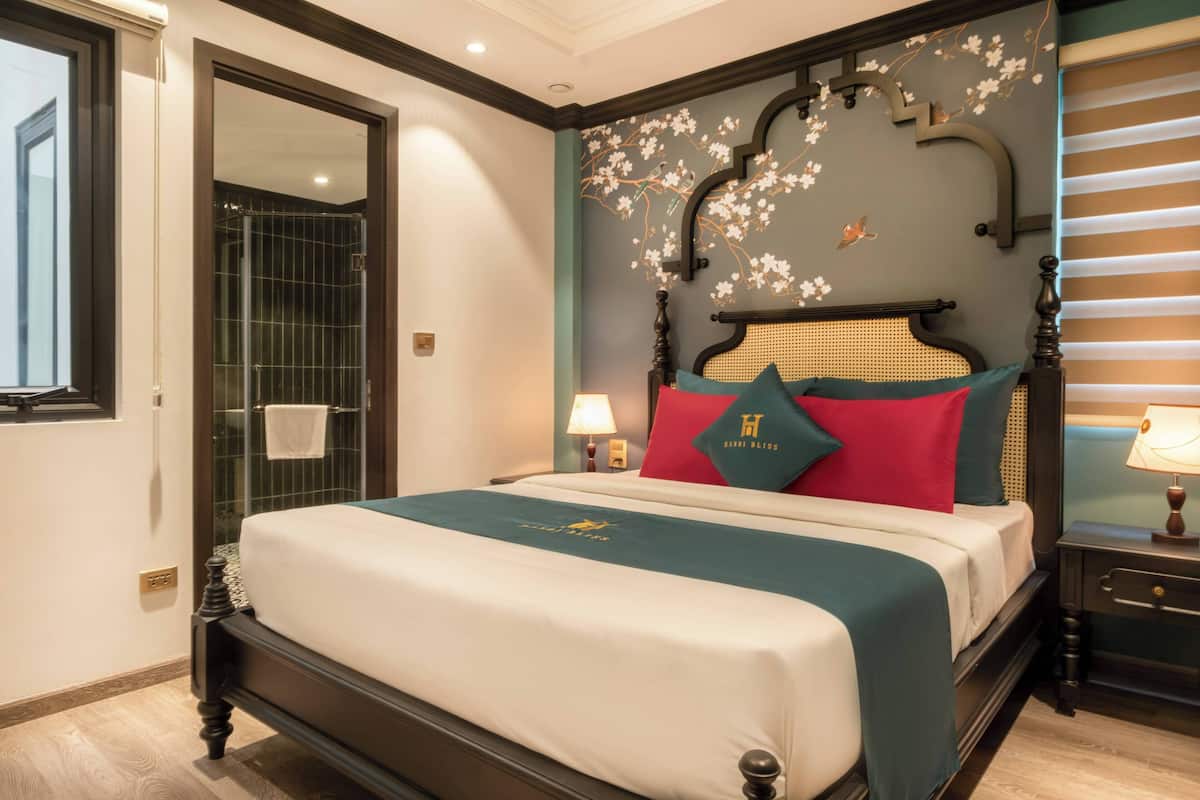 A neatly made bed with a teal bedspread, a wooden headboard with floral designs, and a nightstand with a lamp.