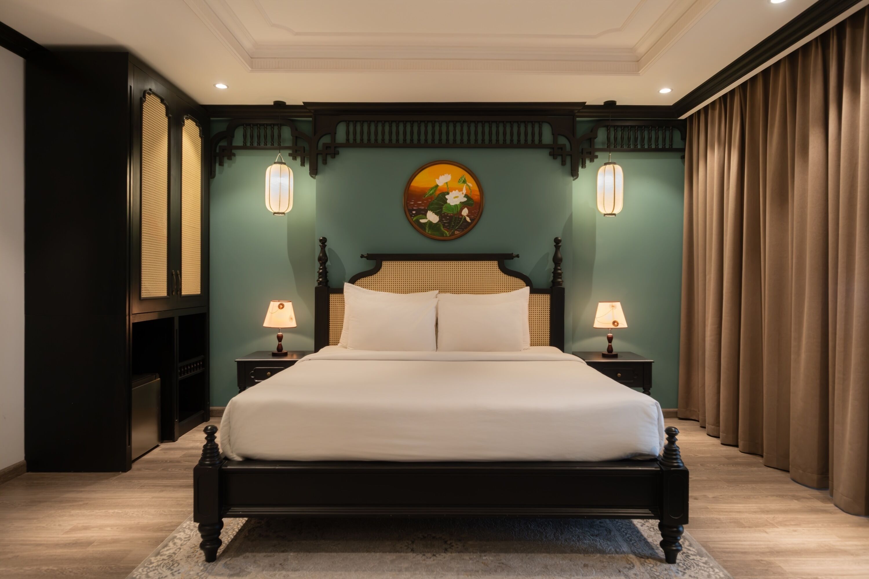 Un grand lit avec un cadre sombre, deux tables de chevet avec des lampes, un tableau accroché au mur et une grande fenêtre avec des rideaux.