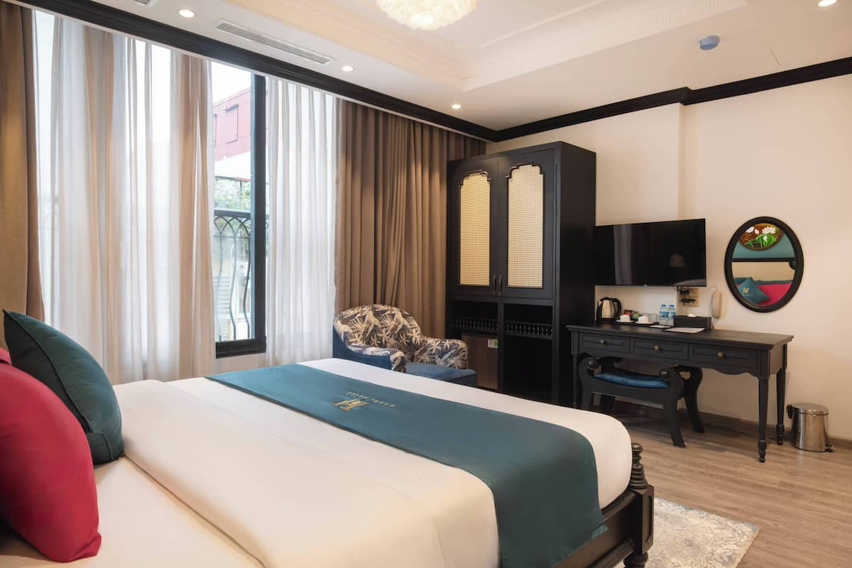 A hotel room with a large bed, a desk, a chair, a television, and a window with curtains.