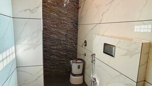 Une salle de bain avec des carreaux de marbre blanc, un mur d’accent en pierre noire, des toilettes, un lavabo et un espace douche.