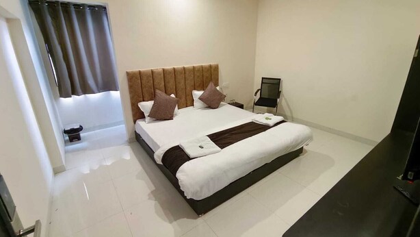 Une chambre d’hôtel avec un lit, un bureau, une chaise, une petite table, un miroir et une fenêtre avec des rideaux.