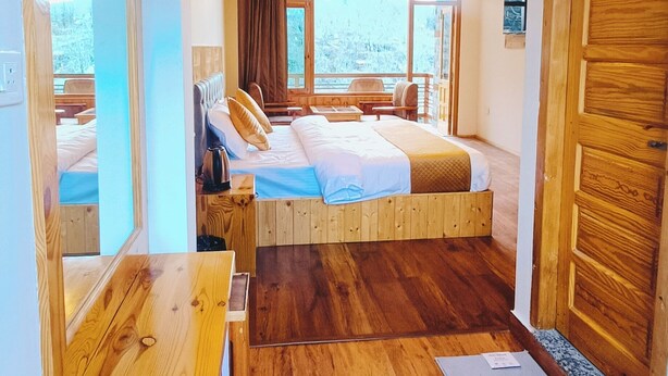 A wooden-floored room with a bed, a desk, and a view of the outdoors. - Hotel Nayra Manali (Manali)