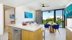 A modern kitchen with a central island, a dining area with blue chairs, and a large window with a city view.