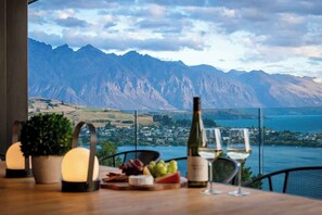 Ein Tisch mit einer Weinflasche und Gläsern, einer Obstplatte sowie Blick auf Berge und einen See.
