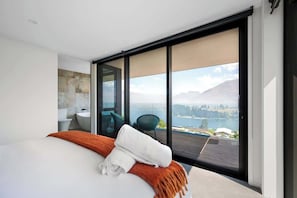 A modern bedroom with a large bed, a view of a lake, and a balcony.