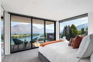 Ein Schlafzimmer mit einem großen Bett, Seeblick und Bergblick, sowie ein Balkon mit Sitzgelegenheiten.