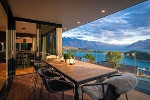 Un espace repas avec une table et des chaises en bois, une vue sur un lac et des montagnes, et un mur en verre.
