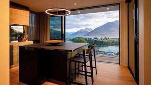 Una cocina moderna con una isla grande, vistas a un lago y montañas, y un comedor con taburetes de bar.