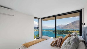 Un dormitorio con una cama grande, vista a un lago y montañas al fondo.