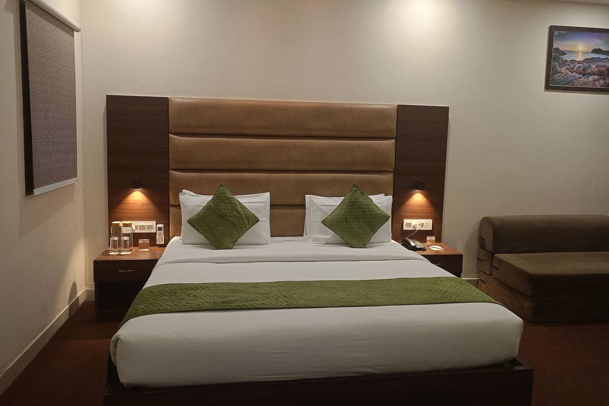 A hotel room with a large bed, two bedside tables, a nightstand, a chair, and a painting on the wall.
