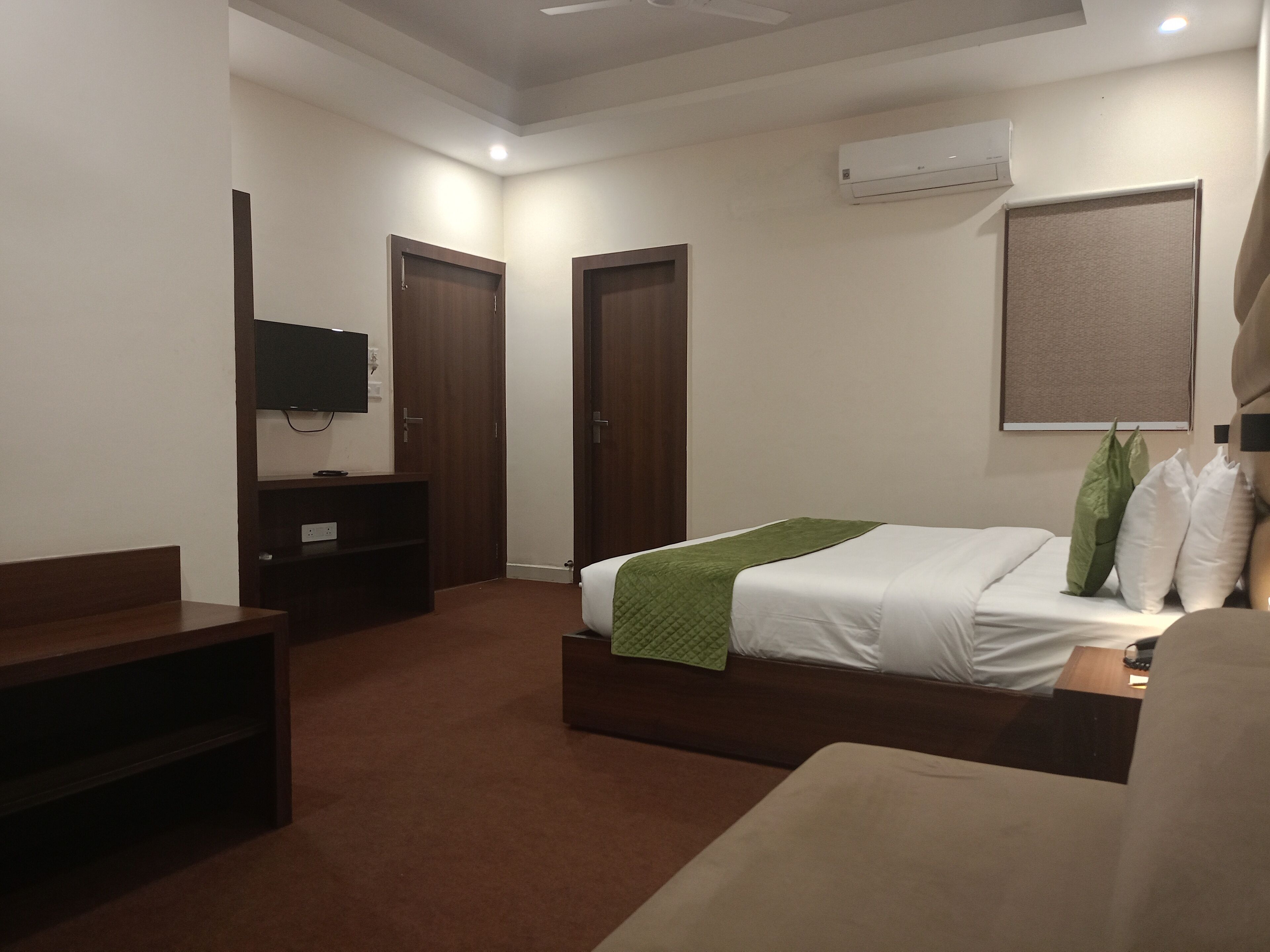 Quarto de hotel com cama, televisão, escrivaninha e guarda-roupa.