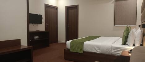 Quarto de hotel com cama, televisão, escrivaninha e guarda-roupa.