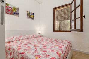 Um quarto com uma cama, uma janela com cortina e duas quadros pendurados na parede.