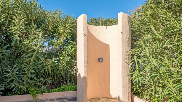 Eine Dusche im Freien mit Steinsäulen und Tür, umgeben von üppigem Grün.