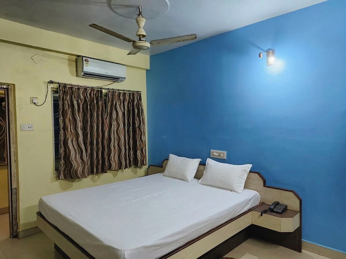 A room with a bed, a ceiling fan, an air conditioner, a telephone, and a curtain.