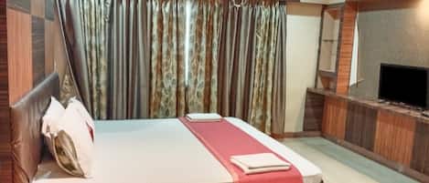 A hotel room with a bed, a television, an air conditioning unit, and a ceiling fan.