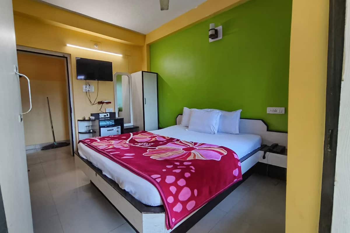 Quarto de hotel com cama, escrivaninha, cadeira, televisão e parede verde.