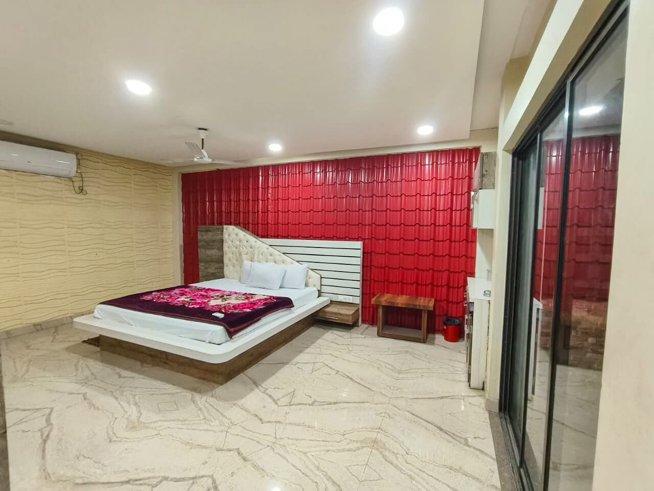 A bedroom with a bed, a nightstand, a bench, a red curtain, and a window.