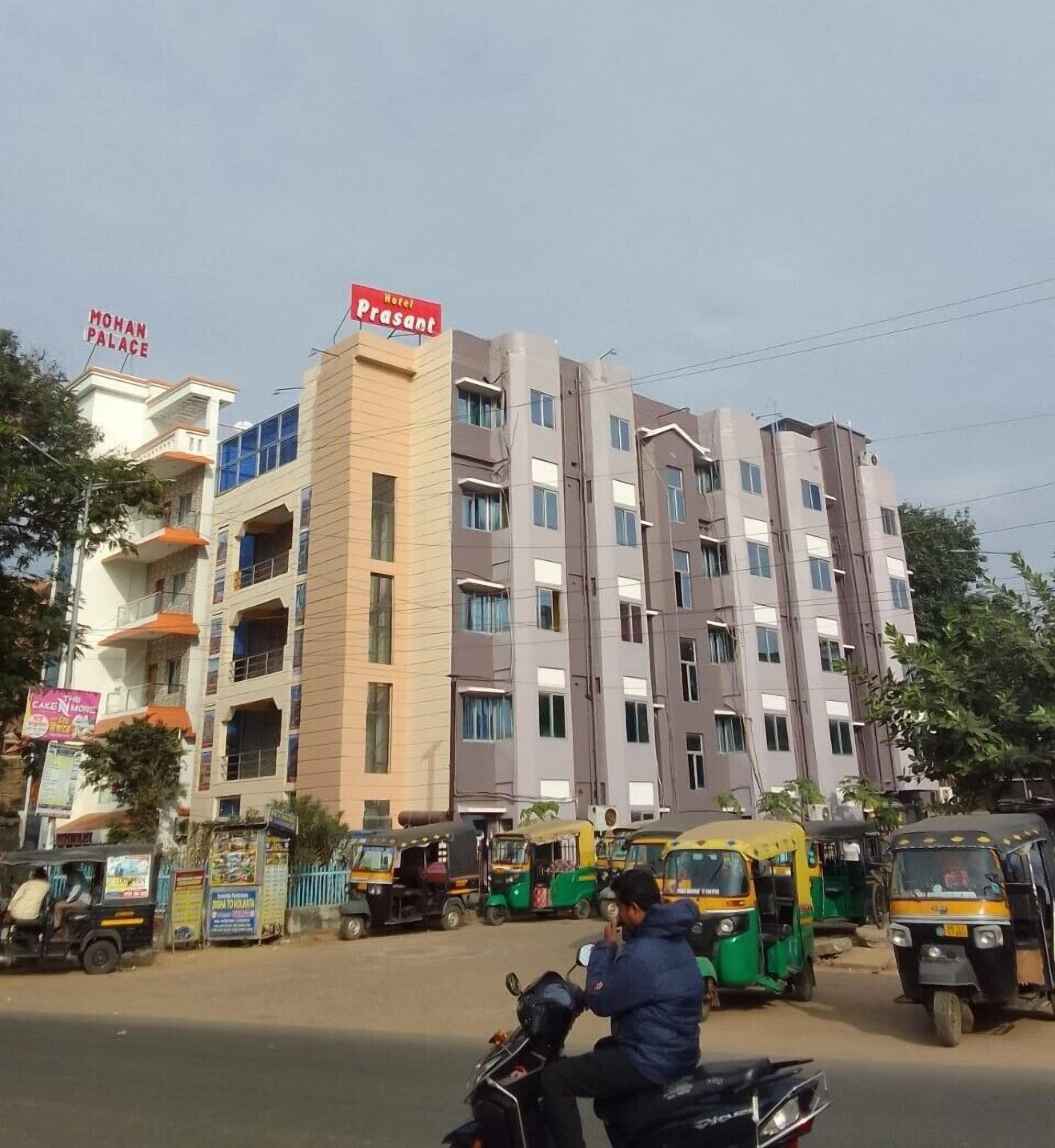 A multi-story hotel with a prominent sign for "Hotel Prasant" and "Mohan Palace" in the background.