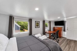 A hotel room with a bed, a desk, a chair, a TV, and a window with curtains. - Pitcher's Paradise Apt 3 - All Star Baseball Rentals (Oneonta)
