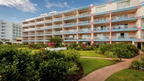 A multi-story hotel with balconies, a garden area with various plants, and a clear sky. - Paradise Perch - Royal Retreats at Maho Beach (Lowlands)