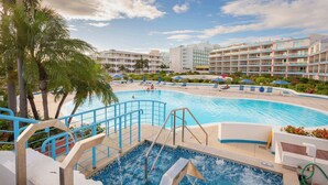 A hotel pool area with a hot tub, lounge chairs, and palm trees. - Paradise Perch - Royal Retreats at Maho Beach (Lowlands)