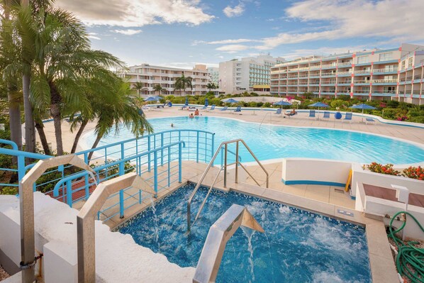 Un área de piscina hotelera con un jacuzzi, sillones de descanso y palmeras.