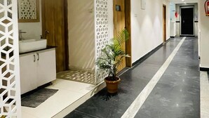 Un pasillo de hotel de diseño moderno, con un panel decorativo blanco, una planta en maceta y una zona de lavamanos con armarios.