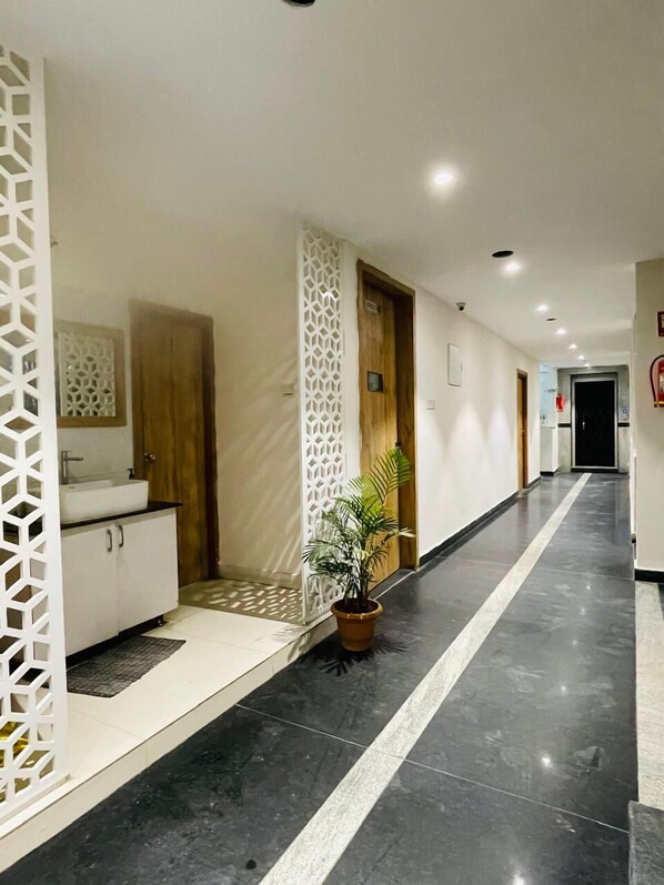 Corridoio di un hotel dal design moderno, con un pannello decorativo bianco, una pianta in vaso e un angolo lavabo con mobili.