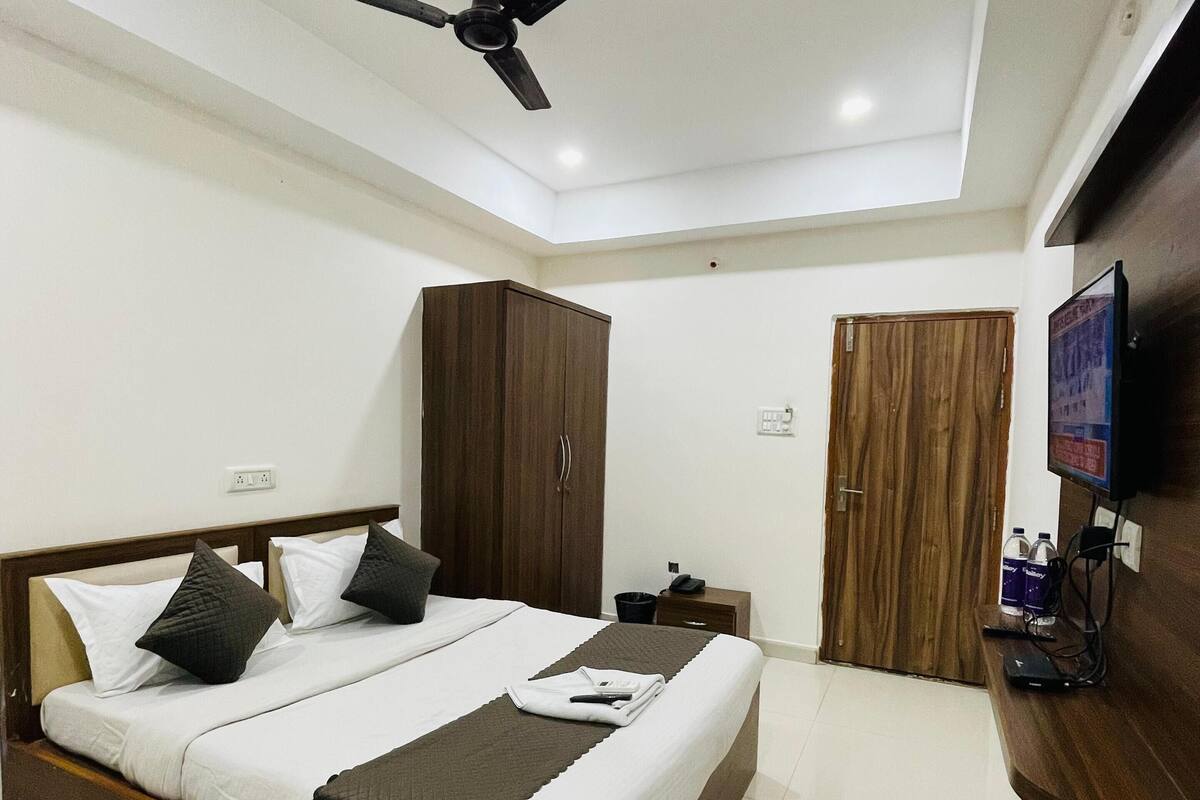 A modern bedroom with a large bed, a ceiling fan, a wardrobe, a TV, and a desk with a computer.