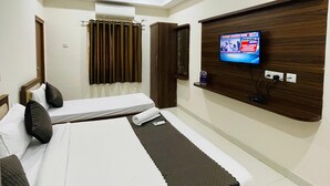 Habitación de hotel con dos camas, ventilador de techo, equipo de aire acondicionado, televisor montado en la pared y cabecera de madera.