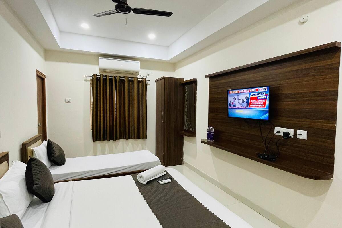 A hotel room with two beds, a ceiling fan, an air conditioning unit, a TV mounted on the wall, and a wooden headboard.