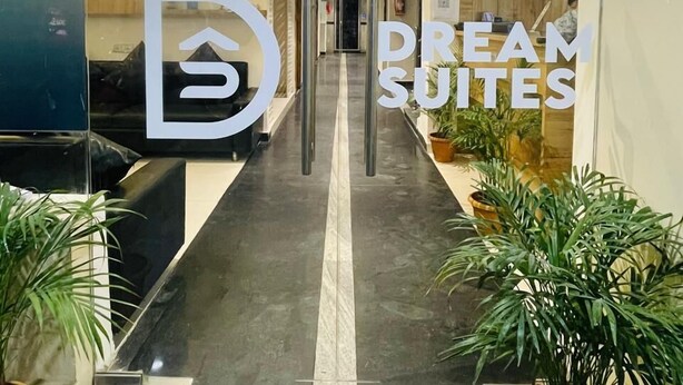 Zona de recepción de un hotel con un mostrador, un cartel de 'PUSH', un cartel de 'NO FUMAR' y plantas en macetas.