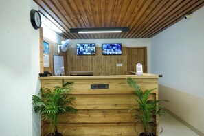 Una reception con piano in legno, due monitor sopra e una sveglia al muro.