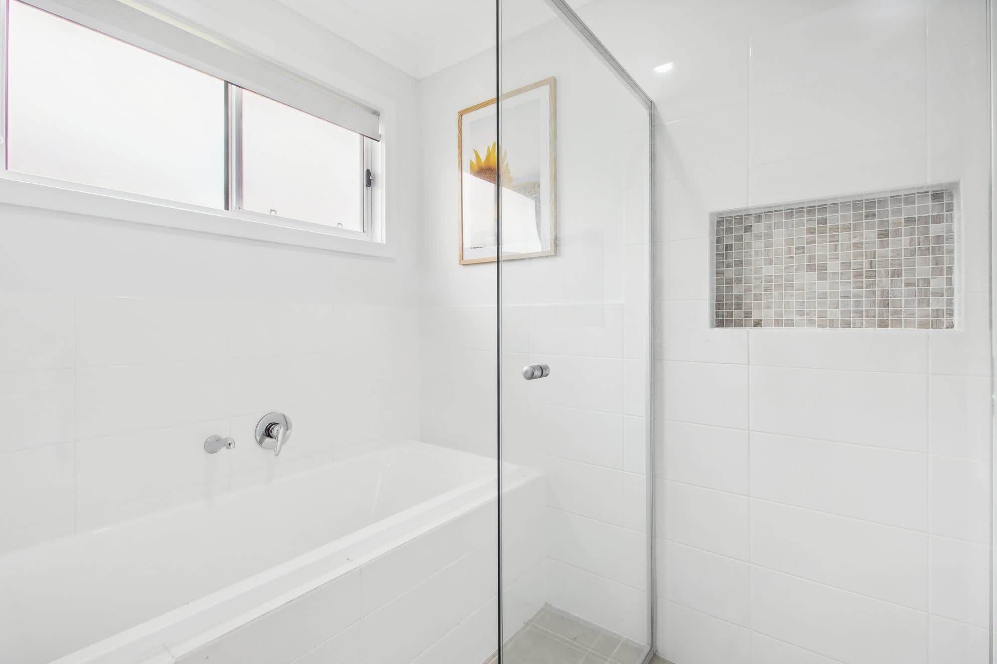 A modern bathroom with a white bathtub, a glass shower enclosure, and a tiled shower wall.