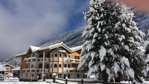 A snow-covered building with a wooden facade and multiple balconies, surrounded by snow-laden trees and mountains in the background. - Mountain Stay With Balcony (Saas Grund)