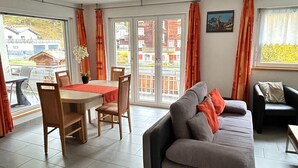 A dining area with a table and chairs, a sofa, and a window with curtains. - Mountain Stay With Balcony (Saas Grund)