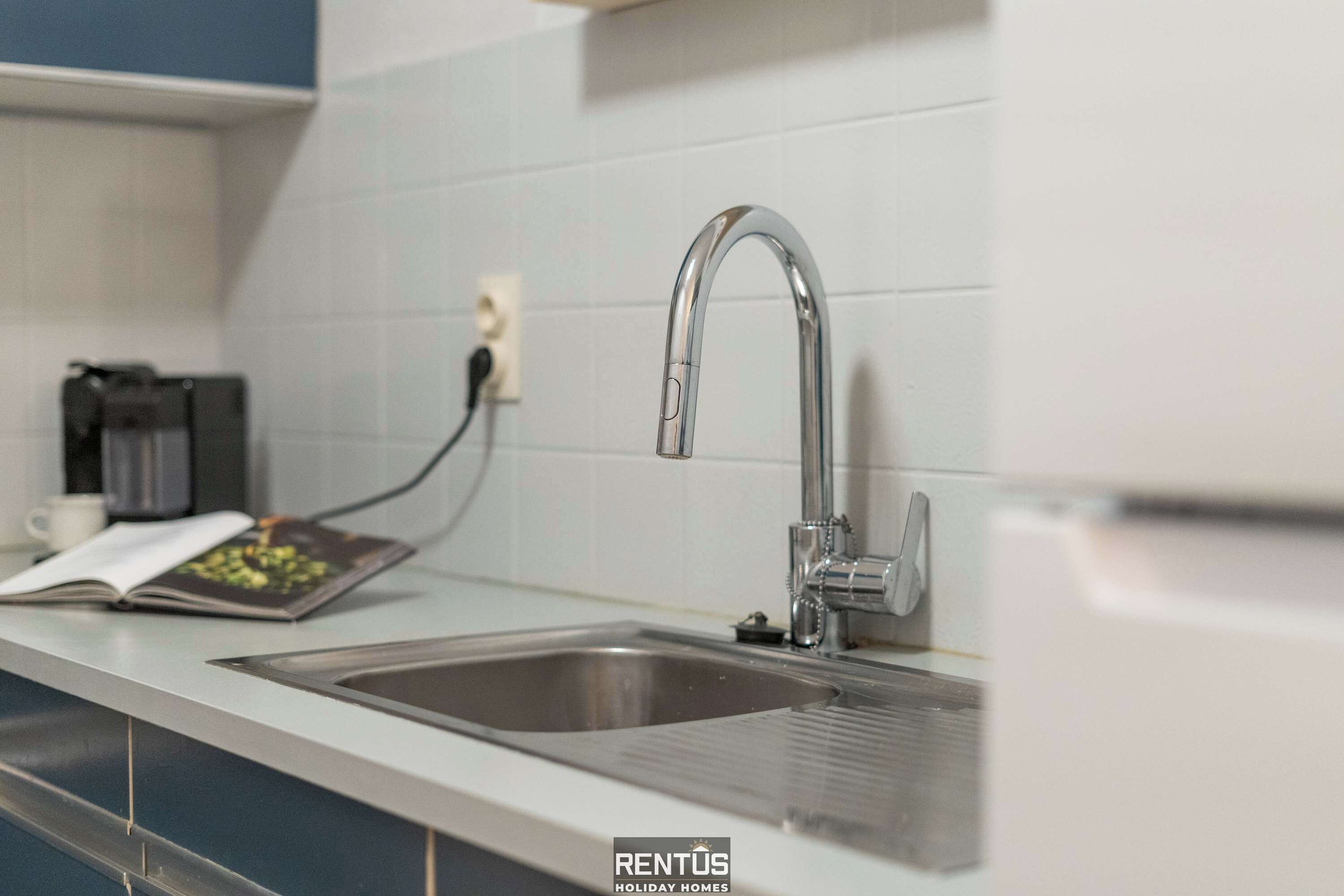 A modern kitchen with a stainless steel sink, a coffee machine, and a power outlet.