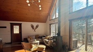 Ein geräumiges Wohnzimmer mit Holzböden und hohen Decken, mit Kamin, Schaukelstuhl und großen Fenstern mit Blick ins Freie.