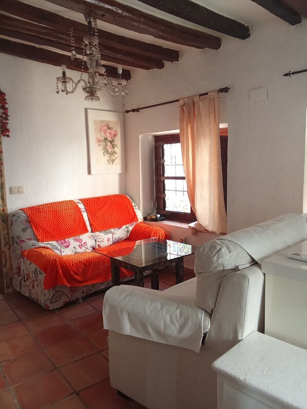 A living room with a floral sofa, a white armchair, a glass coffee table, a chandelier, and a painting on the wall. - Charming 1-bedroom apartment with AC, WiFi in gorgeous Granada (Granada)