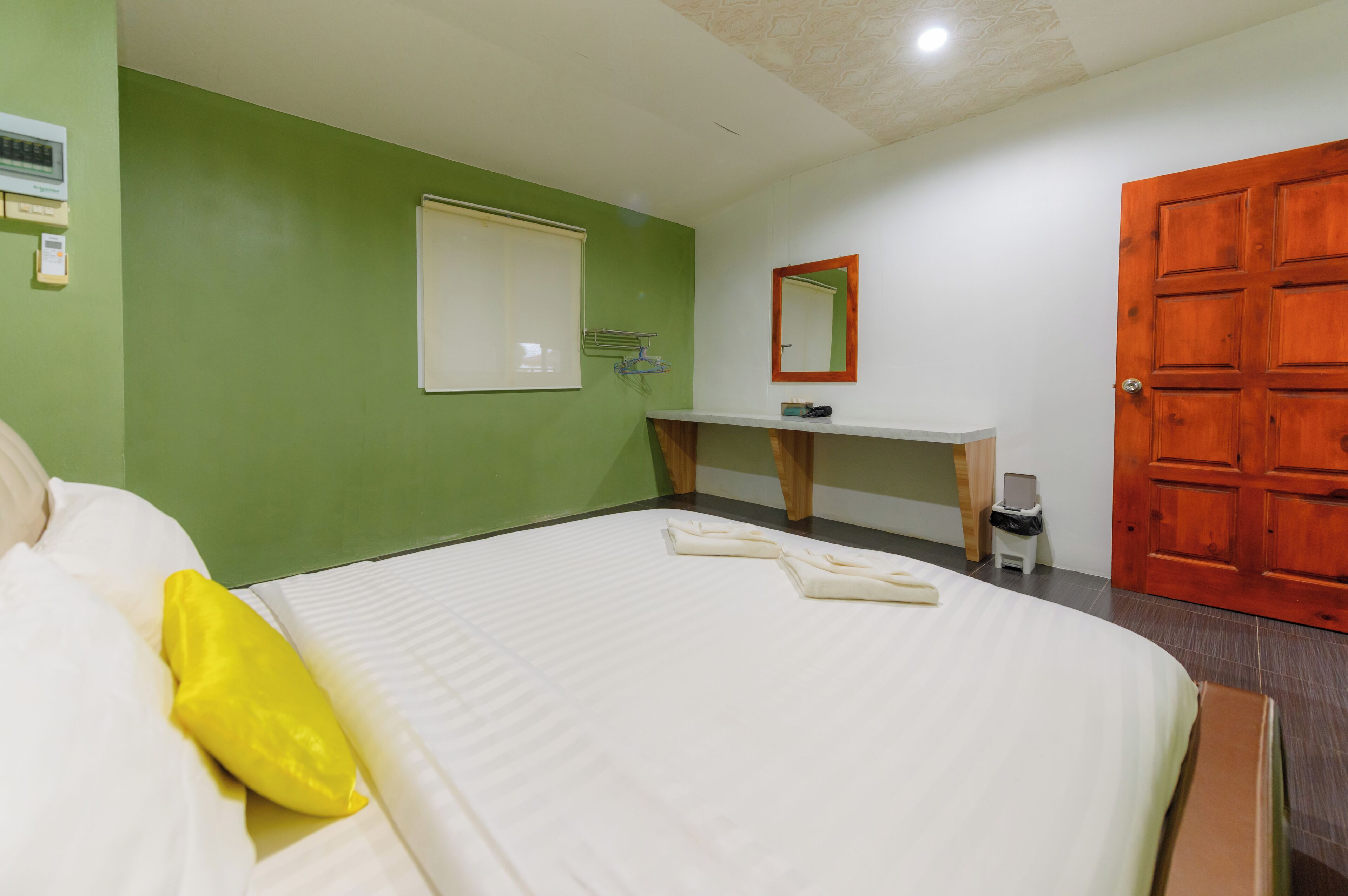 Une chambre d’hôtel avec un lit, un petit bureau, un miroir, une porte en bois et un mur vert.